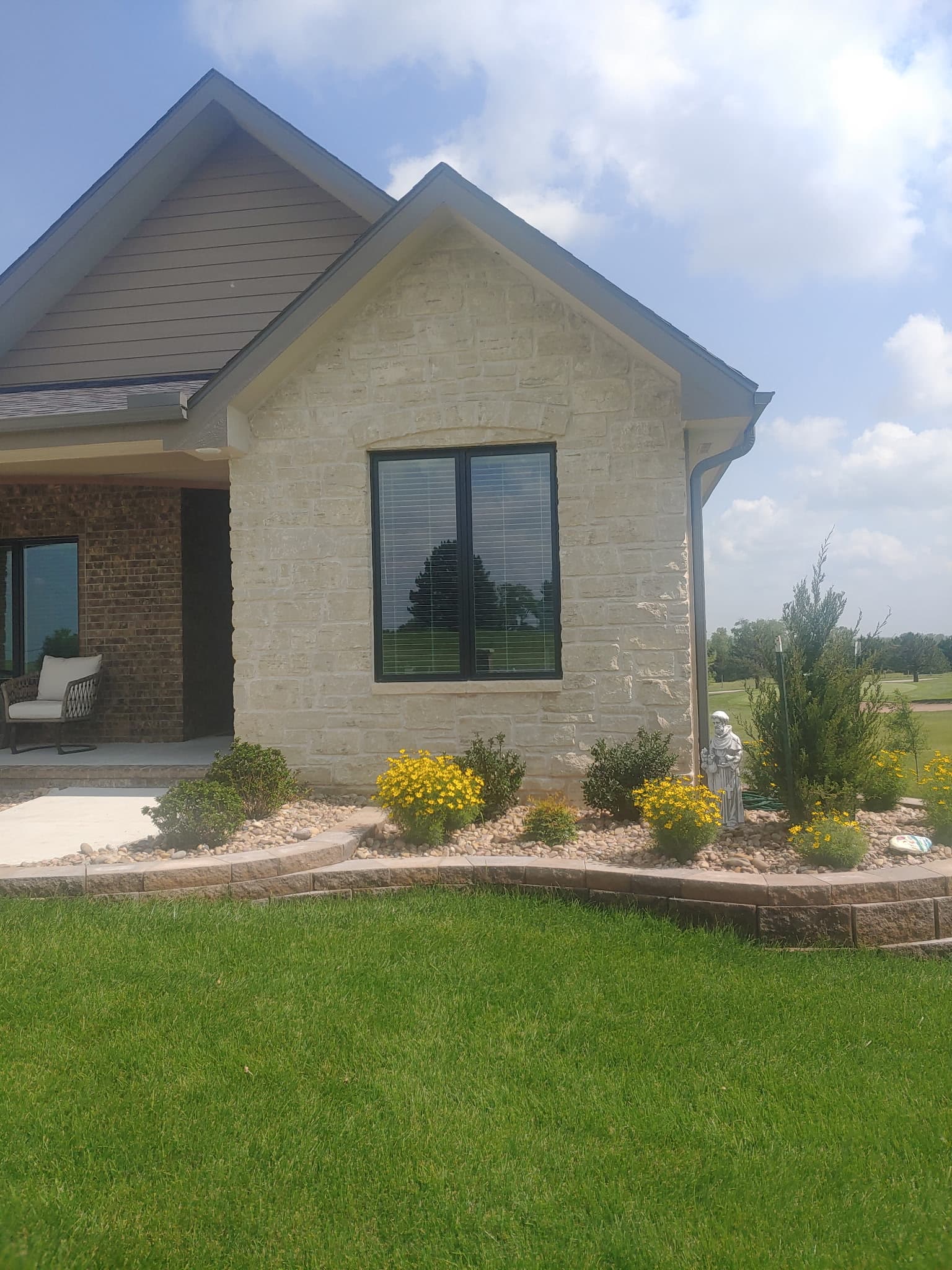 Stone house with a black window and a landscaped garden bed featuring yellow flowers.