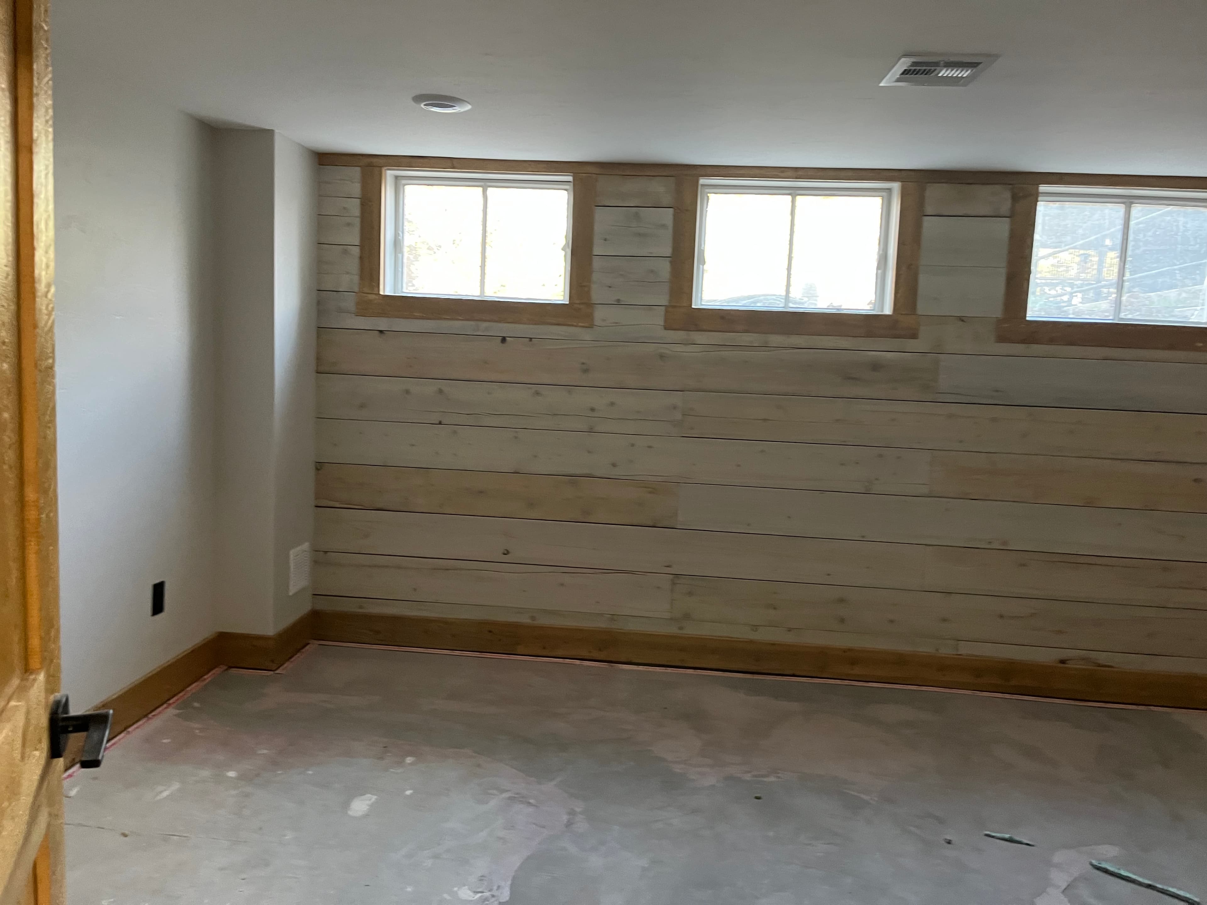 Unfinished room featuring a light wood plank wall with three windows and concrete floors.