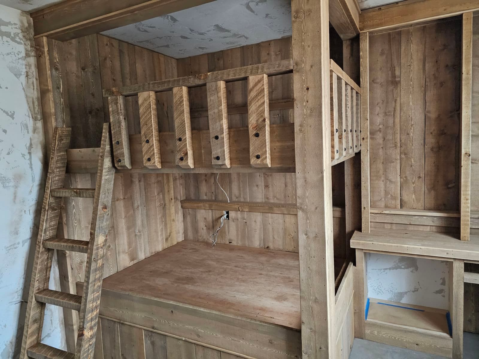 Rustic wooden bunk bed with a built-in ladder and safety rails against paneled walls.